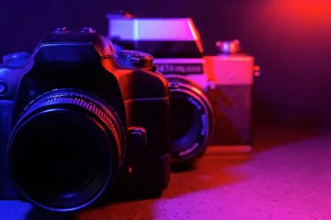 An old camera in front of a modern one in neon red-blue color on a dark backg Stock Photos