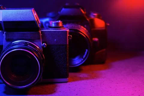 An old camera in front of a modern one in neon red-blue color on a dark backg Stock Photos