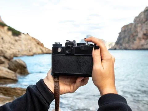 An old camera held by two women's hands on a rocky beach by the sea Stock Photos