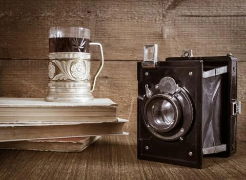 Old camera with tea in coaster and books Stock Photos