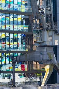 Old cargo crane in front of the glass facade of an office building reflecting Stock Photos