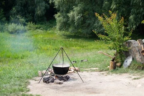 Old cast-iron cauldron on a fire. Cooking food outdoors in a pot on a tripod Stock Photos