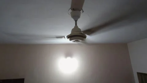 An old ceiling fan hums loudly against a cracked ceiling, illustrating the risin Видео 343784181