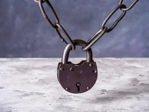 Old chain closed with a rusty padlock hangs above the concrete table Stock Photos