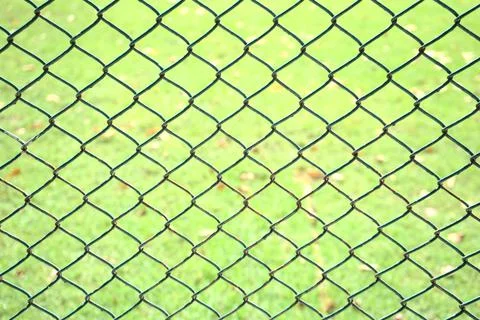 Old chain link pattern abstract fence with green grass field background. Stock Photos