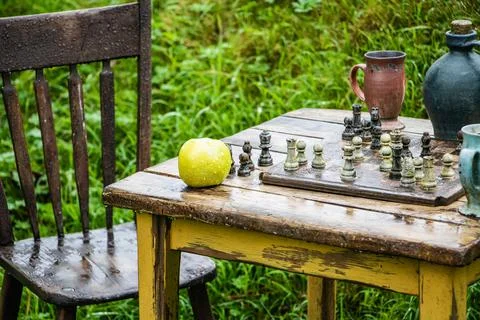 Old chess board and green apple on old wooden table and chair in rain Stock Photos