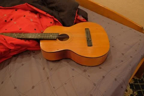 Old classical guitar on a bed in a brown apartment lying on a blanket of re.. Stock Photos