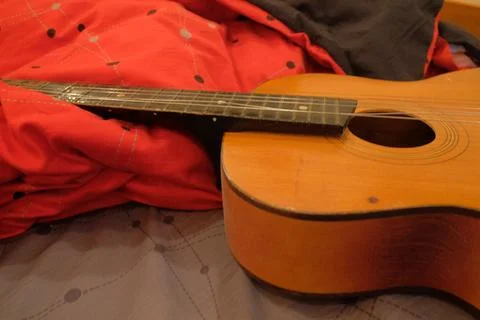 Old classical guitar on a bed in a brown apartment lying on a blanket of re.. Stock Photos