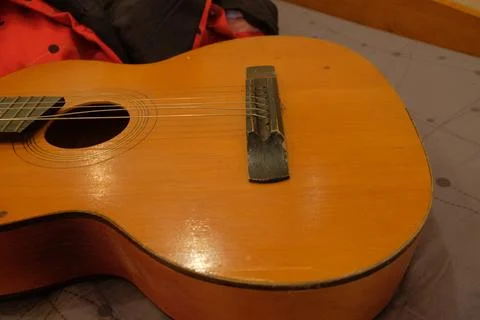 Old classical guitar on a bed in a brown apartment lying on a blanket of red Stock Photos