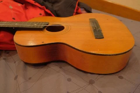 Old classical guitar on a bed in a brown apartment lying on a blanket of red Stock Photos