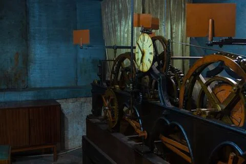 An old clockwork machine with a large clock face and rusty gears in a dimly.. Stock Photos