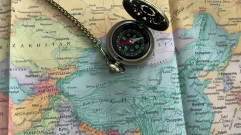 Old compass with a chain resting on a colorful physical map of Asia, focusing Stock Footage 319517126