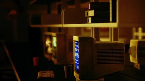 Old computers on desks in a dimly lit room with shelves in view Stock Footage 344994878