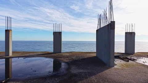 Old concrete pillars stand against a serene ocean backdrop as reflections dance Stock Footage 336484204