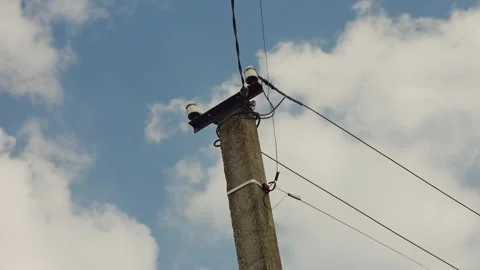 Old concrete utility pole with power lines against a cloudy blue sky Stock Footage 344643127