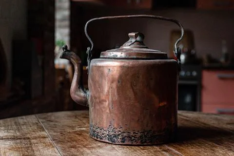 An old copper kettle stands in the kitchen on a wooden table 스톡 사진