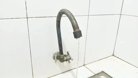 An old, corroded tap is attached to the white tiled wall above the kitchen sink 스톡 동영상 289107396