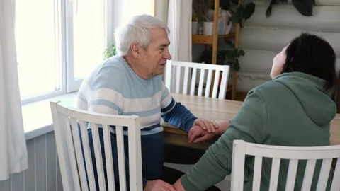 Old couple have breakfast sitting at the kitchen table, drink coffee. Embracing Stock Footage 328620189