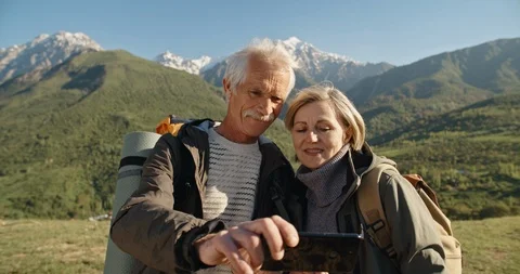 Old couple having a hike in spring mountains, then stopping to take a picture on Stock-Footage 109355323