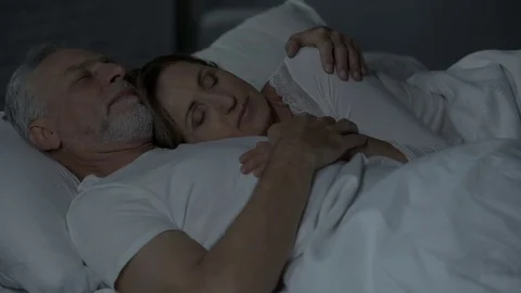 Old couple sleeping in bed, lady lying on male chest, man holding arm around her Stock Footage 79775603