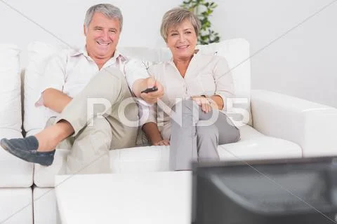 Old couple watching TV with legs crossed Stock Photos