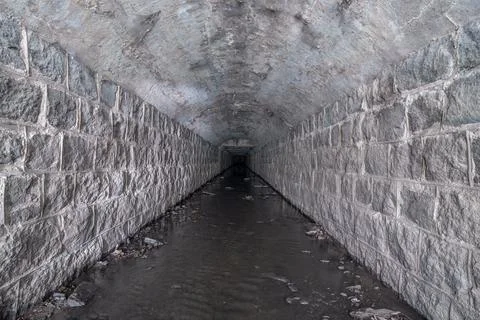 An old culvert or storm drain is built of stone, overgrown with cobwebs. Stock Photos