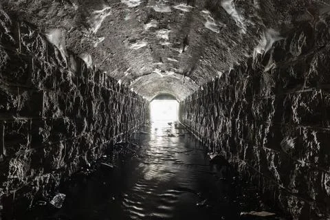 An old culvert or storm drain tunnel with light in the end is built of stone, Stock Photos
