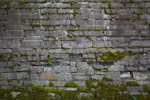 Old dark stone wall with moss as background. Wall cladding with masonry Stock Photos
