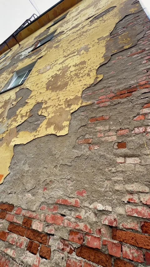 Old decaying building facade with peeling yellow paint and exposed brick wall Video stock 321829512