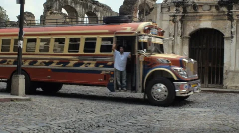 An old decked out school bus drives by the ruins of a church in Antigua Vídeos de archivo 61023180
