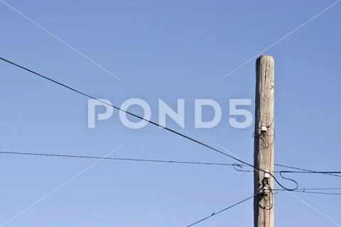 Old decrepit wooden telephone pole against a gradient blue sky. Stock Photos