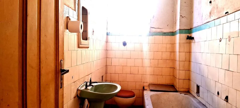 Old dilapidated bathroom interior featuring vintage ceramic tiles and worn Stock Photos