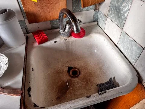 Old dirty kitchen sink with rust stains, red sponge and metal scrubber, con.. 库存照片