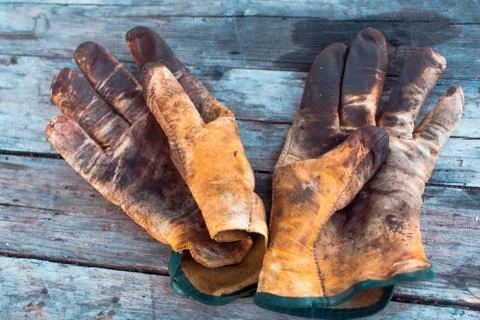 Old dirty work gloves on a wooden table stained with grease and oil. Stock Photos