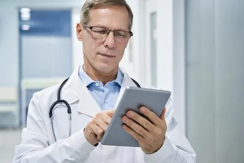 Old doctor using digital tablet e health apps in hospital consulting online. Stock Photos