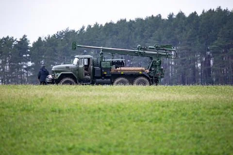 An old drilling machine stands in the middle of a large green field. The cock Stock Photos
