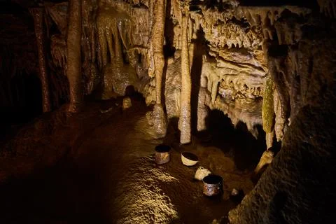Old drinking cups rusting on ground of deep cave surrounded by stalagmites and Stock-Fotos