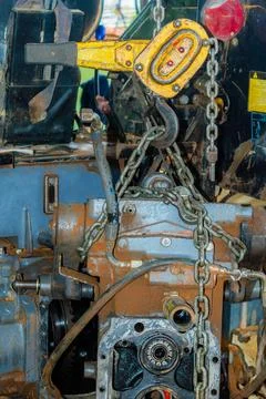 An old, dusty tractor engine hanging from a chain with a pulley. Stock Photos