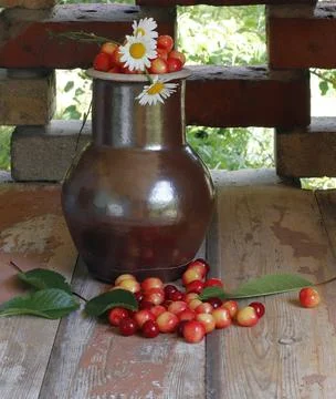 An old earthenware jug is filled with red cherries on an old table. Stock Photos