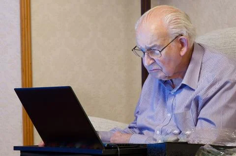 Old elderly senior man using a laptop computer at risk to cyber attack and Photos