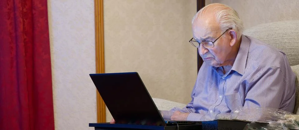 Old elderly senior man using a laptop computer at risk to cyber attack and Stock Photos