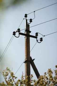 Old electric post on a background of blue sky and trees with leaves. Photos