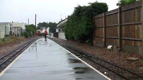 Old English steam train pulling into small railway station very wet Stock Footage 5185982