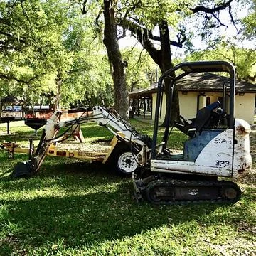 Old Excavator and Trailer on Grass Under Tree Stock Photos
