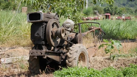 Old farm machine with large wheels stands in a grassy field near trees and dista 스톡 동영상 342140138