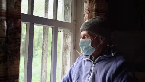 Old farmer wearing warmth cap and medical face mask looking through window Stock Footage 144132362
