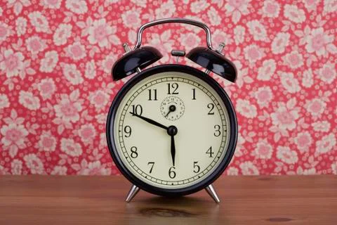 An old fashioned alarm clock in front of floral patterned wallpaper Foto stock