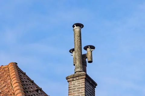 An old-fashioned brick chimney with multiple smokestacks on a tiled rooftop, Stock Photos