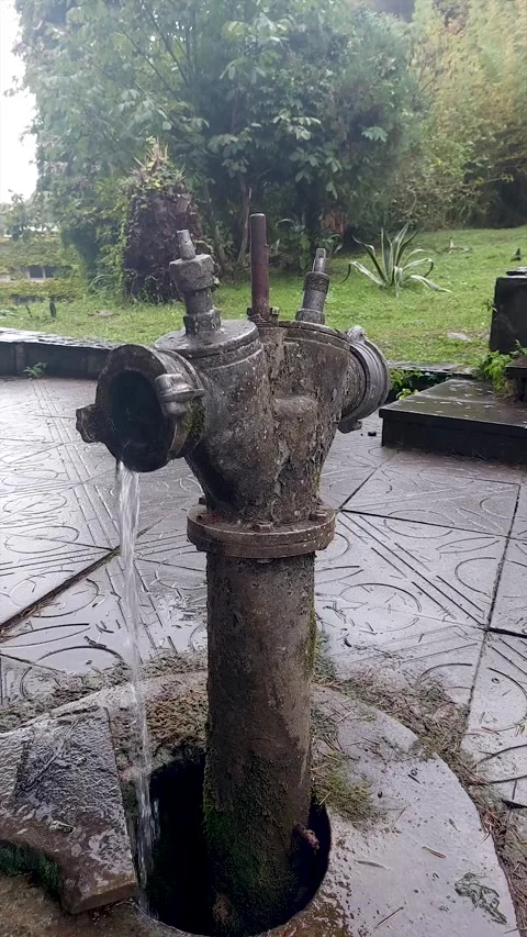 Old-fashioned cast iron water pump column in wet courtyard Stock Footage 337452967