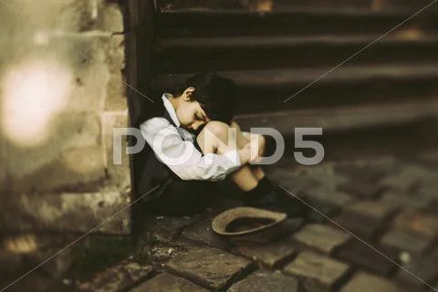 Old-fashioned Caucasian boy sitting near staircase begging for money Stock-Fotos